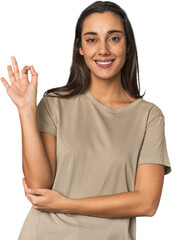 Wall Mural - Hispanic young woman winks an eye and holds an okay gesture with hand.