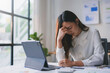 © amnaj - Stressed asian accountant woman suffering from headache while working on laptop computer at office desk