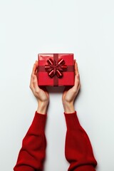 A pair of hands in red sleeves holding a beautifully wrapped red gift box with a bow on a white background.