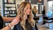 © BajimBa - A woman in a beauty salon whose experienced stylist styles her hair in a fashionable and stylish long wavy ombre with highlights