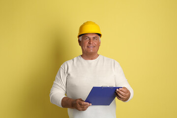 Wall Mural - Engineer in hard hat with clipboard on yellow background