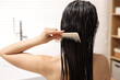 © New Africa - Woman combing her hair with applied mask in bathroom, back view