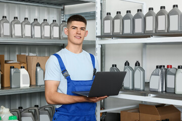 Wall Mural - Smiling young man with laptop and different car products in auto store