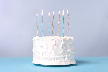 Wall Mural - Tasty Birthday cake with burning candles on light blue table against gray background