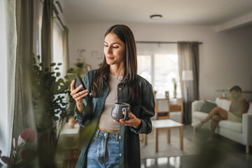portrait of adult young woman stand hold cup and use mobile phone