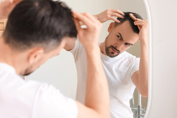 Wall Mural - Handsome man combing hair near mirror at home