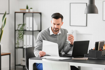 Canvas Print - Handsome businessman working with documents and cup of coffee at table in office