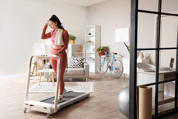 Poster - Sporty young woman wiping sweat on treadmill at home