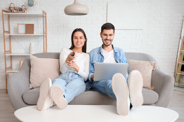 Canvas Print - Happy young couple with laptop and remote control at home