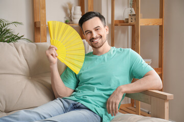 Sticker - Young man sitting on sofa with fan at home