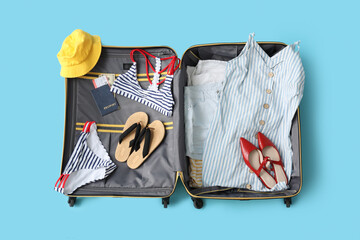 Poster - Open suitcase with belongings and passport on blue background. Travel concept