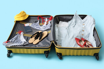 Poster - Open suitcase with belongings and passport on blue background. Travel concept