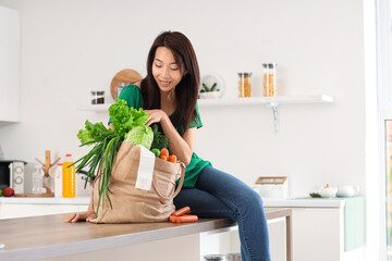 Wall Mural - Young Asian woman with bag full of products in kitchen