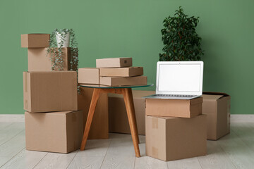 Canvas Print - Blank laptop with moving boxes, table and plants near green wall in room