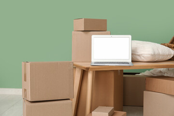 Poster - Blank laptop with pillow on table and moving boxes near green wall in room