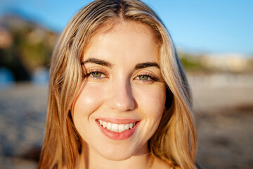 Wall Mural - Portrait of one happy young beautiful woman smiling looking at the camera with big blue and green eyes. Female girl at the beach close up face.