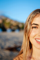 Wall Mural - Portrait of one happy young beautiful woman smiling looking at the camera with big blue and green eyes. Female girl at the beach close up face.