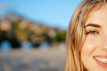 Wall Mural - Portrait of one happy young beautiful woman smiling looking at the camera with big blue and green eyes. Female girl at the beach close up face.