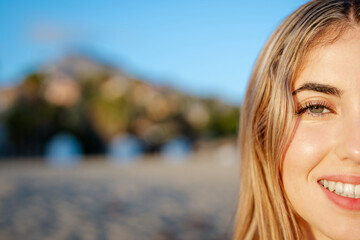 Wall Mural - Portrait of one happy young beautiful woman smiling looking at the camera with big blue and green eyes. Female girl at the beach close up face.