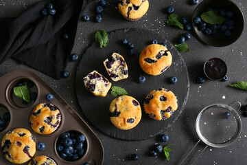 Wall Mural - Baking and stone trays with tasty blueberry muffins on black background