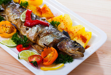 Sticker - Tasty baked whole trout with vegetables, greens and lemon served on white plate..