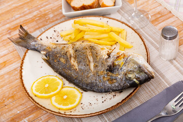 Sticker - Image of a appetizing baked fish called Dorada with French fries, served with sliced lemon pieces