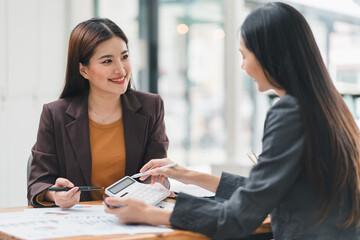 Two businesswomen discussing financial data using tablet and charts at meeting.