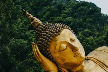 close up of reclining buddha gold statue face with mountain background inthailand.