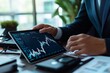 © Jiraphat - A business professional examines financial charts and data on a tablet while seated at a modern office desk, surrounded by technology and greenery during the day