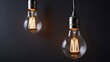 © mischenko - Incandescent lamp glowing on dark gray black wall, copy space. Electricity energy concept, hanging glass technology, illuminated room.