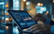 © pimnada - Financial analyst reviewing graphs and charts on a digital tablet in a sleek office environment.,