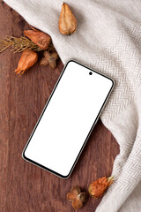 Wall Mural - Mobile phone with blank screen mock up on brown wooden background with neutral beige crumpled fabric and dried orange fall flowers, aesthetic natural autumn business brand template with copy space