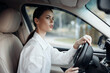© SHOTPRIME STUDIO - Woman driving car, hand on steering wheel, surprised expression at camera, wearing white shirt