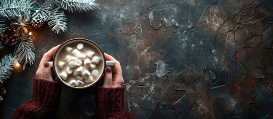 Poster - Flat lay Merry Christmas scene with a female hand holding a cup of hot cocoa with marshmallow on a stone table providing copy space image