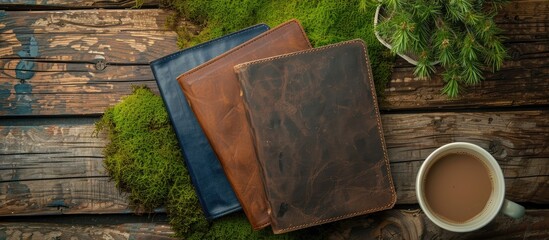 Poster - Top view of a set of hard leather covered diaries or notebooks placed on a wooden surface with a cup of coffee and vibrant green moss providing ample copy space for an image