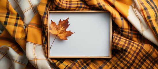 Leinwandbilder - Top view of an empty white board surrounded by autumn themed elements like a maple leaf on a checkered yellow scarf perfect for a copy space image
