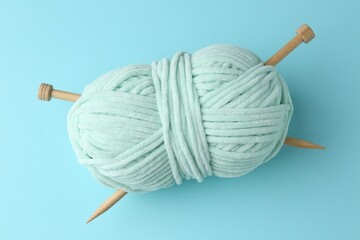 Poster - Plush yarn with knitting needles on light blue background, top view