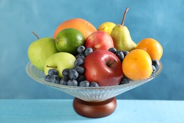 Wall Mural - Glass vase with different fresh fruits on light blue wooden table, closeup