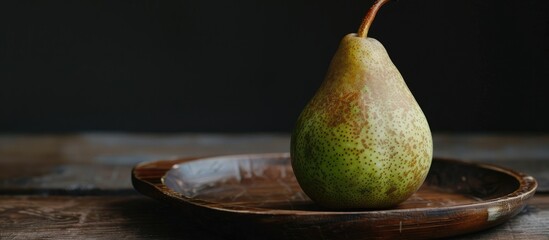 Poster - A raw green pear on a wooden plate against a black backdrop provides ample copy space image