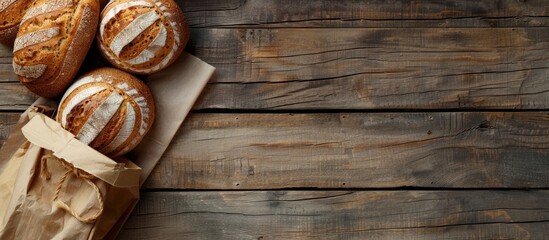 Poster - Fresh bread loaves displayed on a wooden background with a paper bag in a top view copy space image