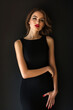 © tynza - Fashionable woman in a sleek black cocktail dress with a minimalist design, posing confidently against a dark, elegant backdrop.