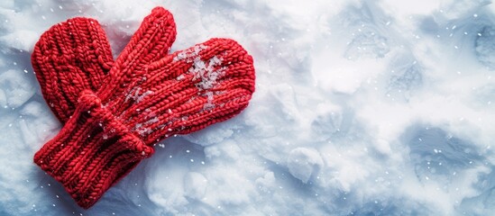 Red mittens lay on snow in a snowy background with copy space image