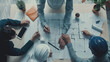 © VK Studio - A collaborative team of professionals actively discussing and drafting architectural plans on a large table filled with blueprints and essential tools.