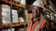 © ChaoticMind - An experienced warehouse worker smiles while wearing a white safety helmet and orange vest, surrounded by stacked packages and shelves, reflecting professionalism and contentment.
