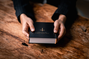 Wall Mural - Hands folded in prayer on a Holy Bible in church concept for faith, spirituality and religion, woman praying on holy bible in the morning. woman hand with Bible praying.