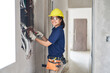 © Robert Kneschke - Portrait of smiling young female electrician using pliers while fixing wires in wall at incomplete house construction site