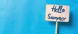 © Ilgun - Summer greetings portrayed with a wooden stick displaying Hello Summer against a blue paper backdrop embodying a fresh business lifestyle with room for a copy space image