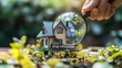 © niti - Hand with a magnifying glass over a tiny house, symbolizing detailed mortgage inspection and valuation