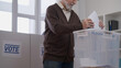 © Synthex🇺🇦 - Close-up of an elderly man casting a ballot paper into a vote container at a polling station