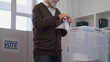 © Synthex🇺🇦 - Male voter putting a paper ballot in a box at a polling station, transparent elections